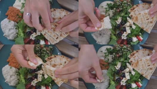 手打破皮塔饼，蘸上鹰嘴豆泥。餐盘上有沙拉、蘸酱和皮塔饼。健康的中东有机烹饪高清在线视频素材下载
