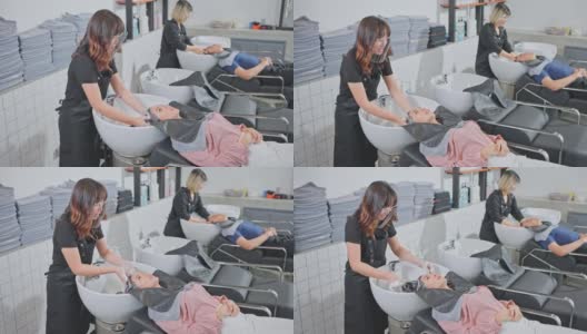 亚洲年轻的女人和男人躺在发廊洗床，在发廊里由发型师洗头。顾客在交谈和放松的同时，美发师按摩和洗头用水。高清在线视频素材下载