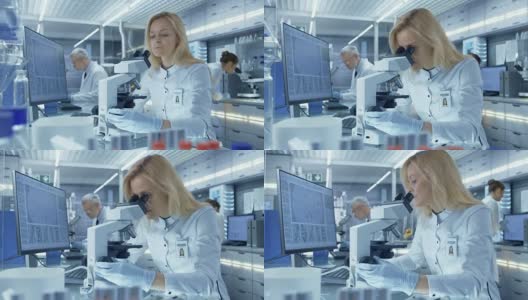 女性研究科学家在显微镜下观察生物样本。她和她的同事们在一家大型现代化实验室/医疗中心工作。高清在线视频素材下载