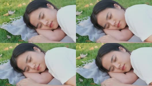 缓慢的动作年轻的亚洲女人睡觉，而躺在地面公园在春天，夏天，特写亚洲女孩午睡和躺在花园户外休息的背景，女性青少年休息，放松，幸福健康的生活方式高清在线视频素材下载