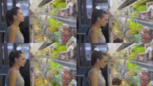妇女在有机蔬菜部冰箱里挑选生菜。购买健康的素食高清在线视频素材下载