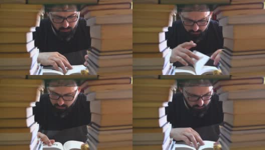 一个留着胡子、戴着眼镜的男人在一堆书中寻找信息。高清在线视频素材下载