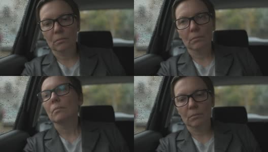 一个忧心忡忡的女商人，戴着眼镜，在雨中等在车里，望着窗外高清在线视频素材下载