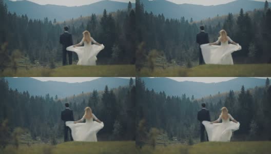 一对年轻美丽的新婚夫妇一起站在山坡上，看着美丽的山林景色。慢动作高清在线视频素材下载