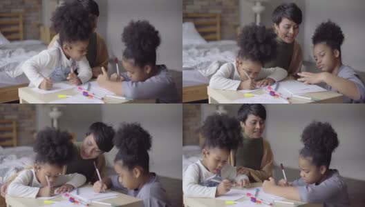 亚洲母亲帮助她的两个非洲女儿和教绘画作业在公寓高清在线视频素材下载
