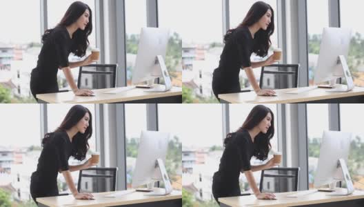 在办公室里，年轻的女商人用电脑站在办公桌前喝咖啡高清在线视频素材下载