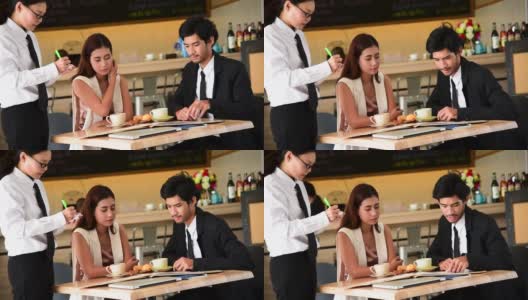 2月14日情人节，一对情侣在餐厅点餐。服务员注意到顾客点餐时，看着菜单有微笑的服务心。情人节的概念。高清在线视频素材下载