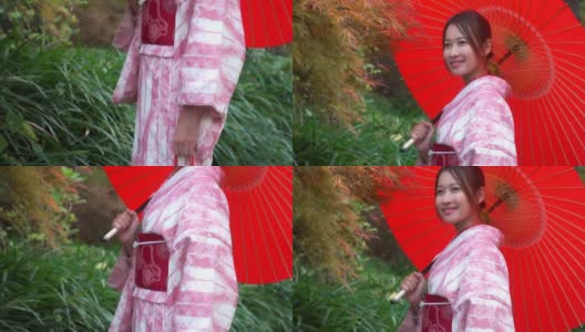微笑的年轻美丽的亚洲女性游客穿着粉红色的传统日本和服拿着红色的伞放松和享受旅游假期在东京城市的公共公园，日本高清在线视频素材下载
