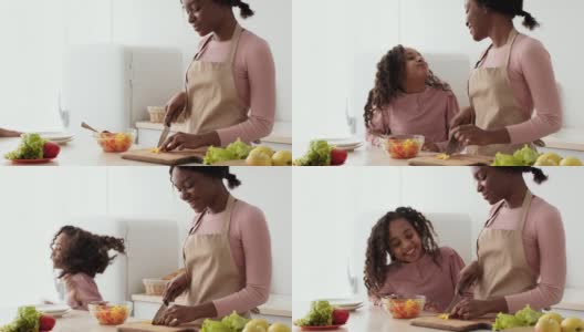 年轻的非洲裔美国母亲正在准备蔬菜沙拉，卷曲的小女儿走了过来，在厨房吃着新鲜的胡椒高清在线视频素材下载