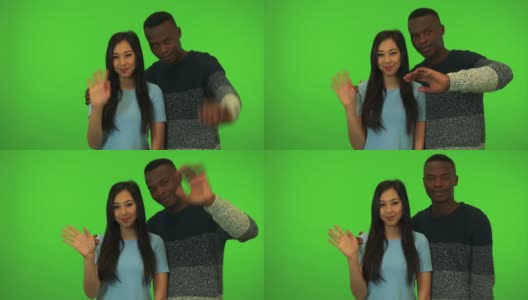 一个年轻的亚洲女子和一个年轻的黑人男子微笑着向镜头挥手——绿幕摄影棚高清在线视频素材下载