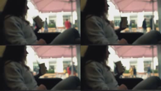 散焦的黑发女孩坐在窗前，用吸管在咖啡馆喝她的饮料。全高清背景散景剪辑高清在线视频素材下载