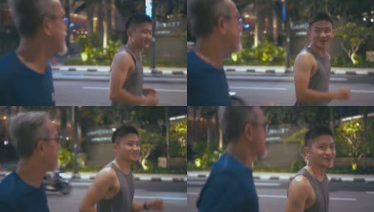 侧观亚洲华人活跃的老人和他的儿子晚上下班后一起在城市跑步慢跑高清在线视频素材下载