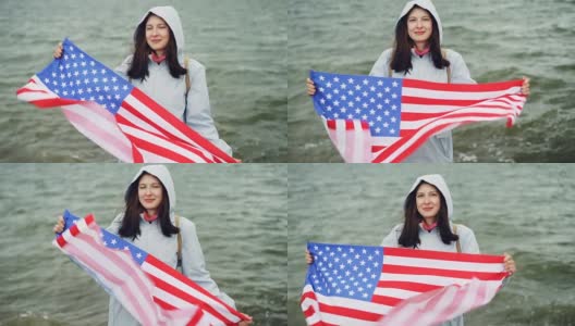 慢动作肖像快乐的美国女孩举着美国国旗和移动它站在海岸边与波浪可见。国籍和国家概念。高清在线视频素材下载