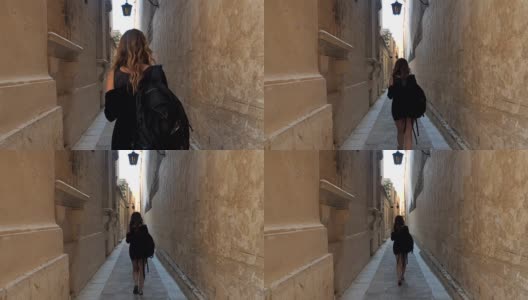 一个年轻女孩走在城市街道的老区的后视图高清在线视频素材下载