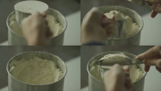 一个年轻女人的手用一个金属量杯从罐子里舀面粉，然后用菜刀去除顶部多余的面粉高清在线视频素材下载