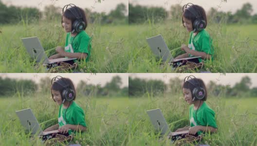 小女孩戴着耳机，在绿草地上用笔记本电脑社交媒体。乡村景色。在夏天的休闲时间高清在线视频素材下载