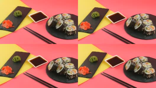 阴阳寿司卷上有鳗鱼和红色的鱼鲑鱼，时髦的珊瑚黄色背景板，黑色的板，绿色的芥末和粉红色的姜。极简主义风格的日本料理高清在线视频素材下载