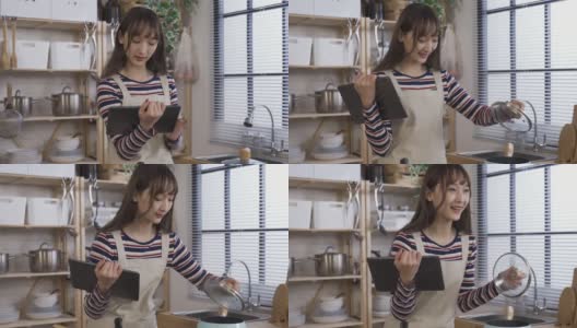 在网上学习用触控板做饭的亚洲女孩，在白天打开锅盖，闻到家里厨房里的香味，感到很开心。高清在线视频素材下载