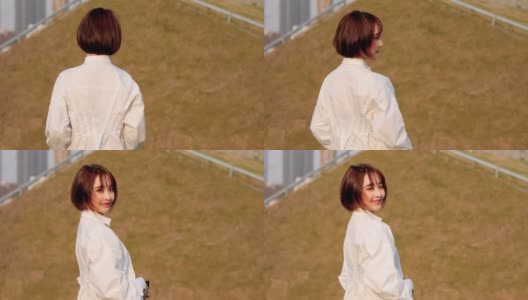 在风和日丽的日子里，穿着白衬衫的美丽中国女孩回头对着镜头微笑，甜美的微笑和可爱的眨眼，4k电影，慢动作。高清在线视频素材下载