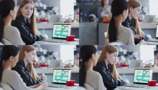 在咖啡馆的桌子上，一位红发女商人正在电脑屏幕上看亚洲设计师设计的网站模板高清在线视频素材下载