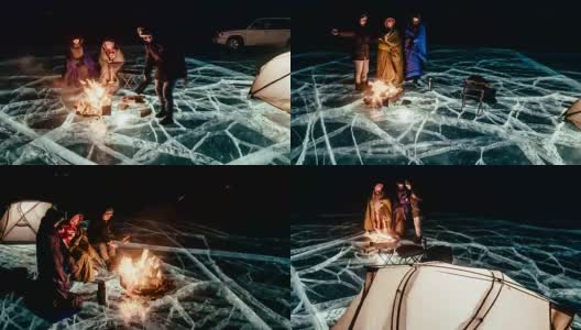 三个旅行者站在篝火旁，就在夜晚的冰面上。营地冰。帐篷紧挨着火。人们正在火炉旁取暖。延时与圆周运动。贝加尔湖。高清在线视频素材下载