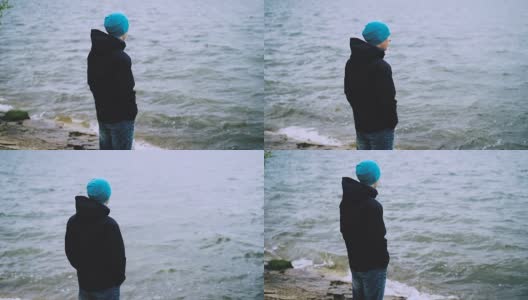 慢动作肖像体贴的家伙在帽子，夹克和牛仔裤站在海边，看着海浪享受自然。健康的生活方式和旅游理念。高清在线视频素材下载