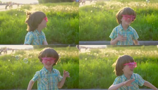 快乐的小可爱的男孩在公园里玩肥皂泡的特写。在夏日阳光明媚的日子里，孩子们在外面玩耍跳舞，快乐的假期，假期，童年，夏天，眼镜高清在线视频素材下载