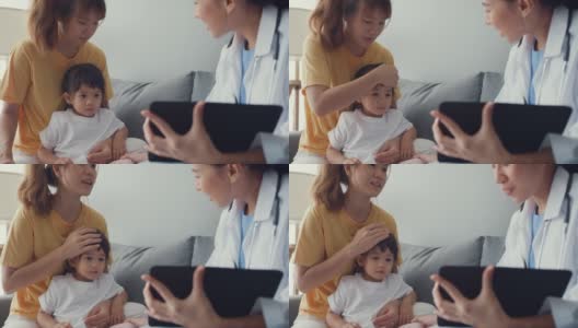 年轻的亚洲女儿科医生和小女孩病人使用数字平板电脑分享良好的健康测试消息与快乐的妈妈坐在沙发在家里。高清在线视频素材下载