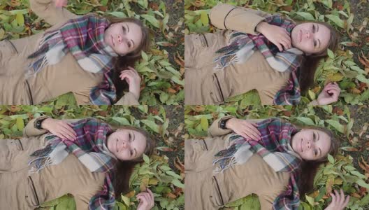 一个穿着大衣的年轻女子躺在秋叶上。微笑的幸福高清在线视频素材下载