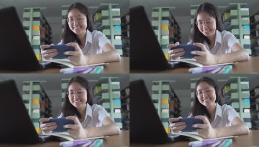 亚洲大学生女孩读书，工作和网上购物与笔记本电脑和智能手机在公共图书馆做她的家庭作业高清在线视频素材下载