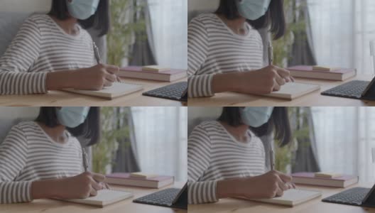 亚洲女孩的手正在做作业和使用平板电脑。亚洲妇女戴着防护口罩在家感染流感或COVID-19。健康与疾病概念高清在线视频素材下载