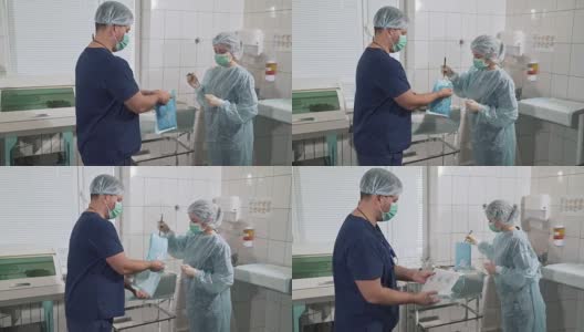 一名女外科医生从包裹中拿出一件无菌的晨衣。一队戴着口罩的医生正在为手术做准备。医疗器械。健康理念，在医院工作。诊所设备高清在线视频素材下载