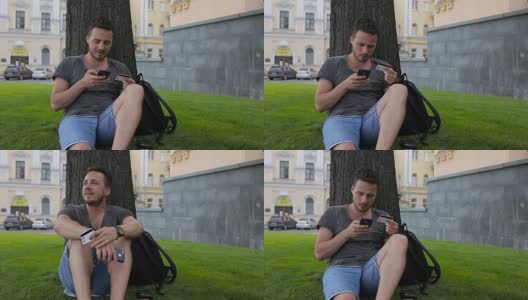 男子用信用卡在网上购物时用智能手机在公园的一棵树下坐着高清在线视频素材下载