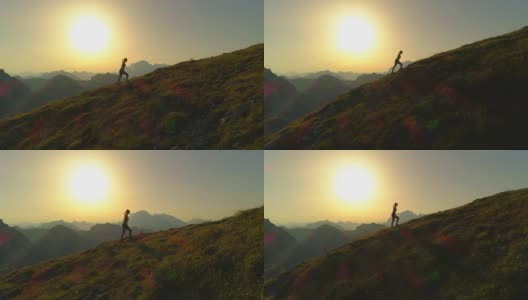 空中剪影:日落时分，一个年轻女子爬上一座山的剪影。高清在线视频素材下载