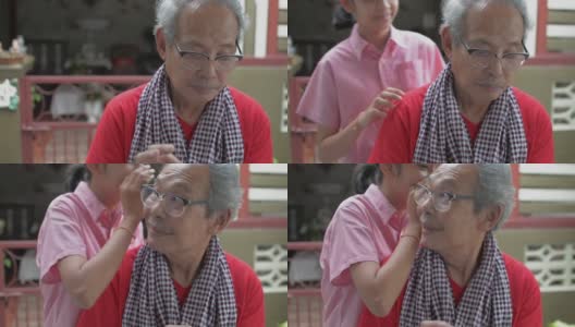 亚洲的老爷爷穿着便装在家里和朋友在智能手机上聊天，他可爱的孙女过来在他耳边兴奋地低语。高清在线视频素材下载
