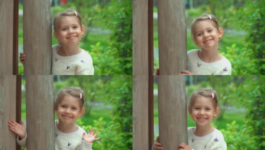 在绿色的夏日公园里，小女孩看着相机，笑了起来。快乐的孩子在户外玩耍。孩子在操场上的院子里高清在线视频素材下载