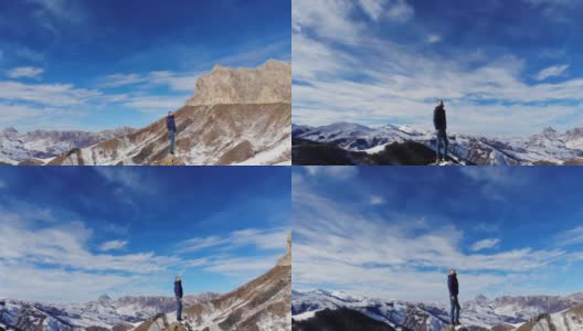 鸟瞰图，年轻的白种人胡子时尚的人站在一块大石头上，在风景如画的雪山覆盖的岩石。晴天，蓝天白云高清在线视频素材下载