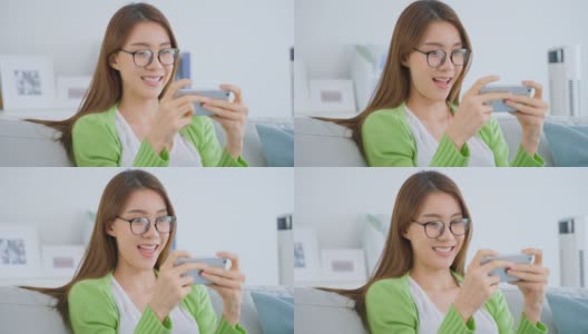 亚洲美女戴眼镜，在家用手机聊天。有吸引力的年轻女孩坐在沙发上，感觉兴奋和快乐后使用智能手机检查在客厅的好消息。高清在线视频素材下载