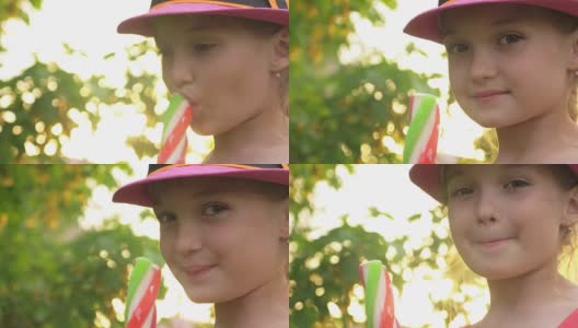 戴着帽子的小孩舔冰淇淋。女孩正在吃美味的冰淇淋。五颜六色的草莓味棒冰是孩子们夏天最爱吃的菜。高清在线视频素材下载