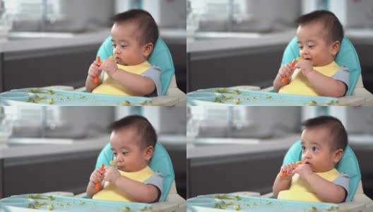 宝宝看了看手里的胡萝卜。第一次吃泥。他的亚洲小男孩的母亲喂养婴儿食品。高清在线视频素材下载