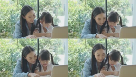 一位亚洲母亲喜欢用笔记本电脑教她可爱的女儿做作业。亚洲小女孩喜欢和她漂亮的妈妈一起学习。高清在线视频素材下载