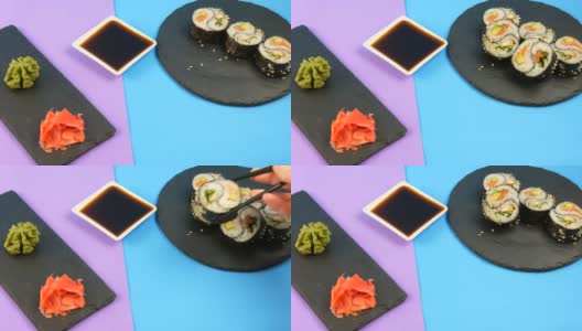 黑色的木条将阴阳寿司卷与鳗鱼和红色的鱼鲑鱼放在时尚的紫蓝色背景板，绿色的山葵和粉红色的姜。极简主义风格的日本料理高清在线视频素材下载