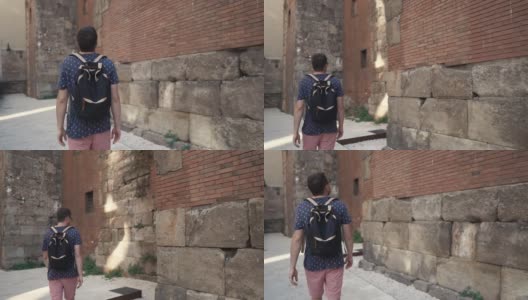 夏日里，一个年轻人正沿着古老的中世纪建筑墙走着高清在线视频素材下载