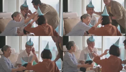 亚洲华人男子帮助他的父亲戴上派对帽，准备在家里的客厅庆祝生日高清在线视频素材下载