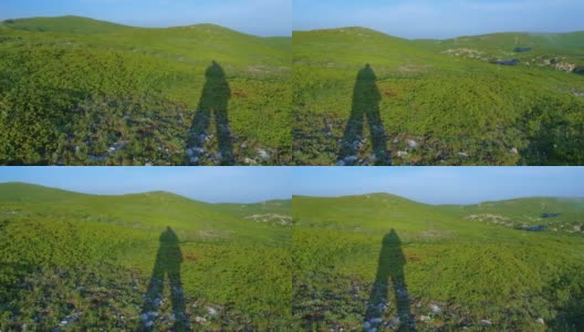一个旅行者的影子在一个高山草地和蓝天的背景上。高清在线视频素材下载