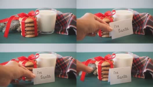 给圣诞老人的圣诞饼干。女人的手上放着一条短信，上面写着“送给圣诞老人”，旁边放着一杯牛奶、饼干、松枝和餐巾。高清在线视频素材下载