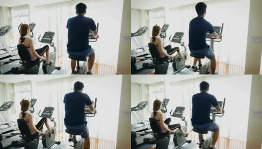 年轻的健身夫妇使用自行车运动自行车在健身房，有氧训练的概念高清在线视频素材下载