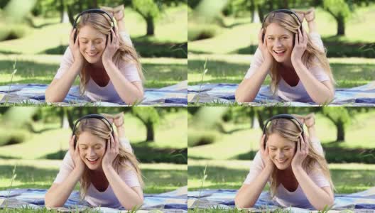 快乐的女孩躺在毯子上在公园听音乐高清在线视频素材下载