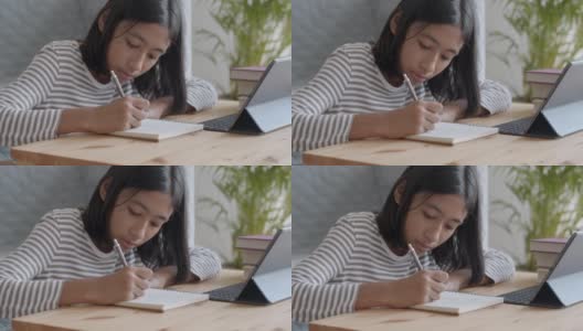 手持。一个亚洲女孩正在做作业，早上在桌子上用平板电脑。在家在线学习概念高清在线视频素材下载
