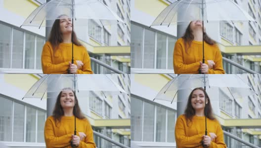 幸福的年轻女子在雨中站在透明的伞下，背景是一幢公寓高清在线视频素材下载